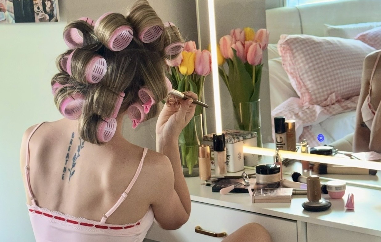 Starra getting ready at her vanity with pink hair rollers and tulips